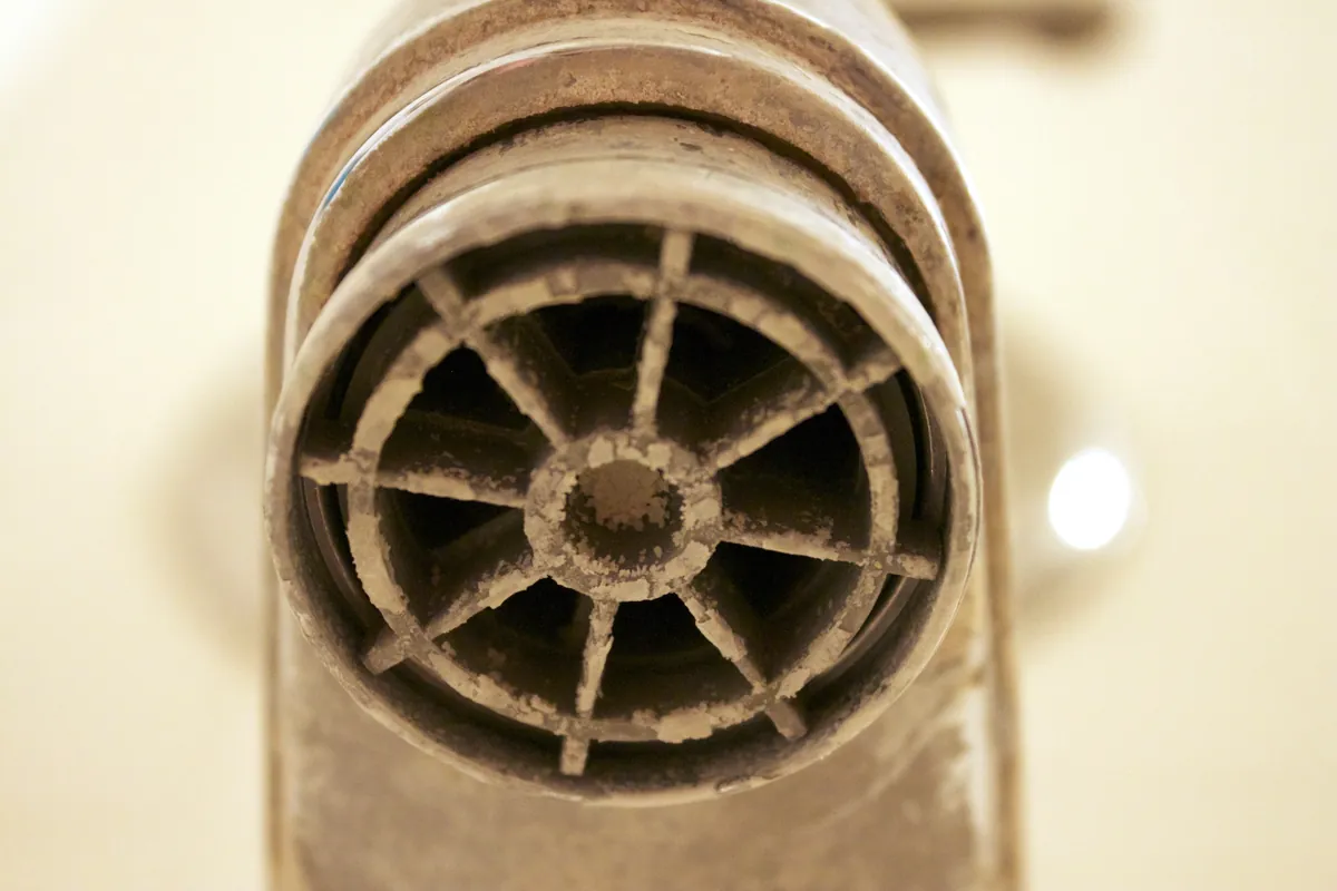 Close-up of a faucet outlet crusted with pale mineral scale around its screen.