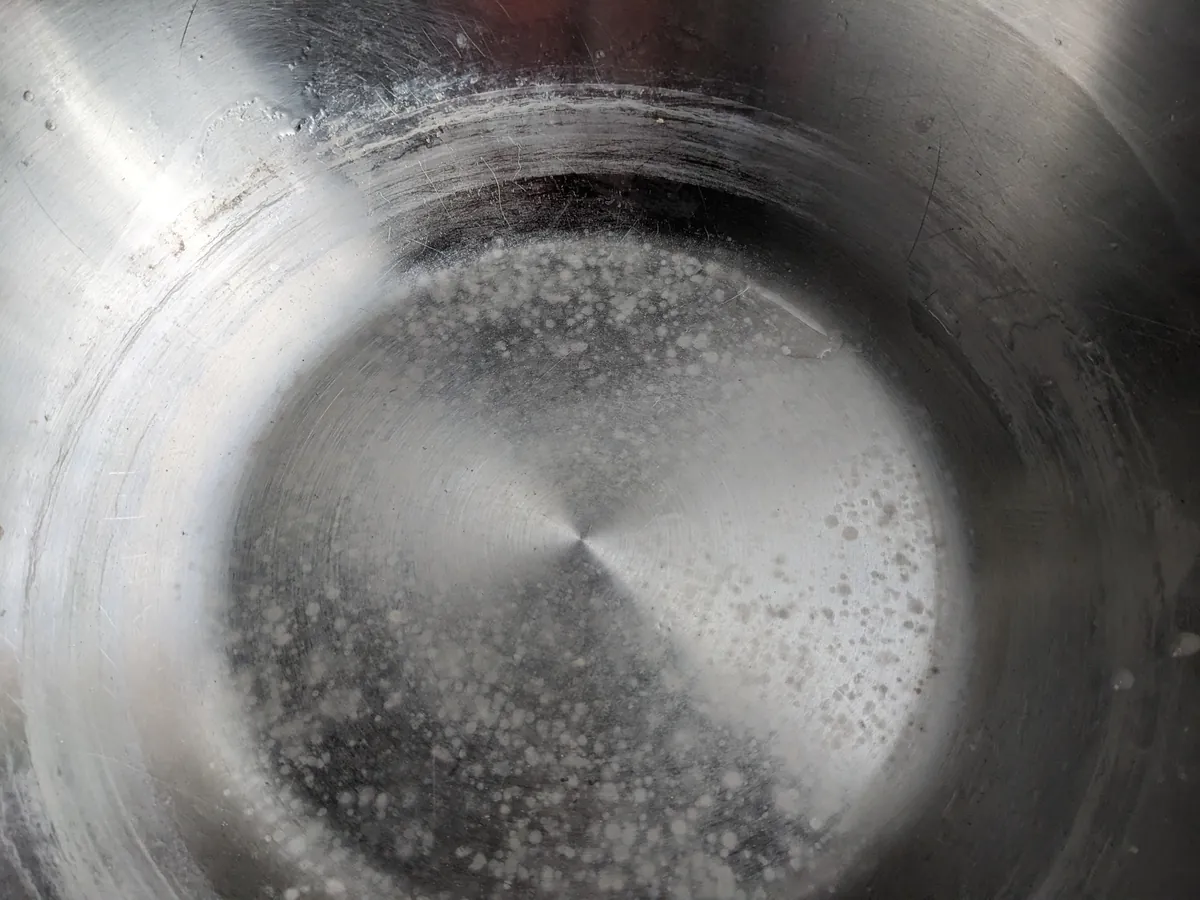 Inside of a stainless steel cooking pot with white limescale spots and rings on the bottom.