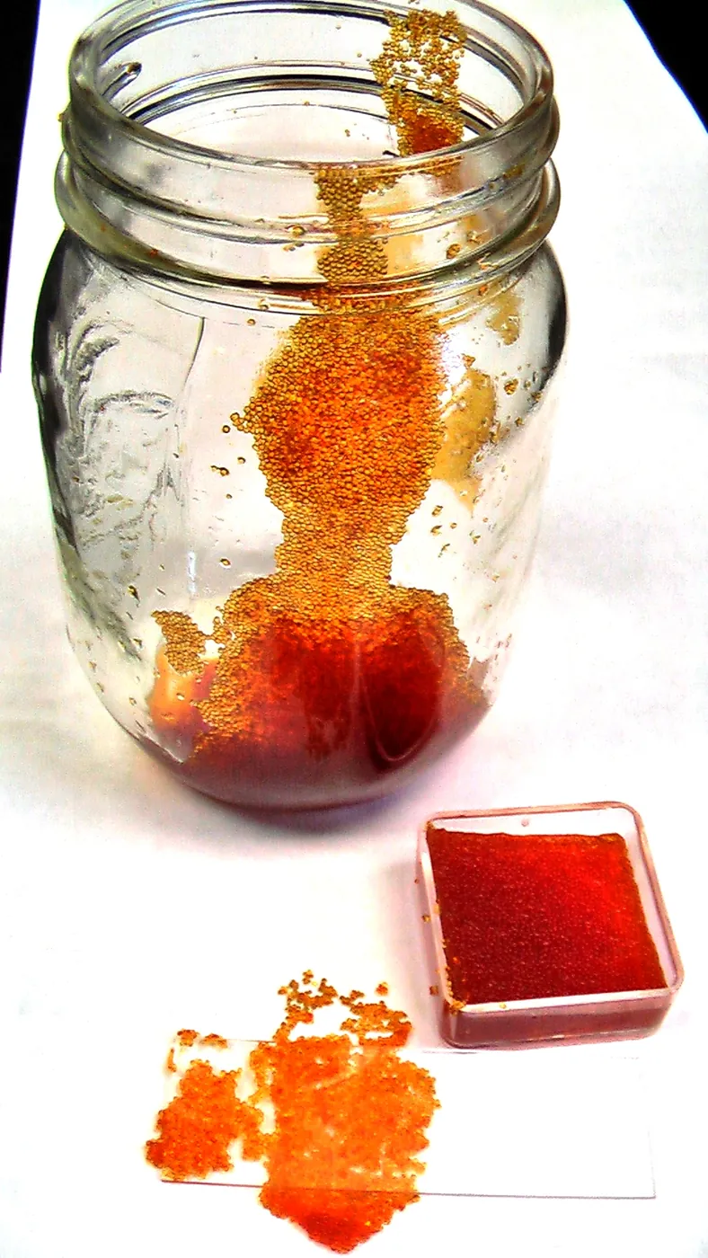 A glass jar and a small dish holding orange-brown resin beads, with more beads spilled on a white surface.